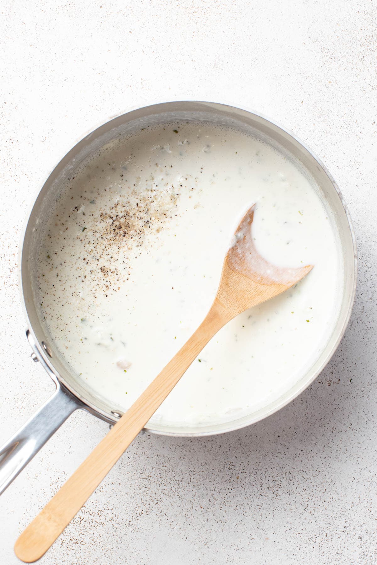 A wood spoon dipping into the creamy, cheesy sauce in a stainless pan.