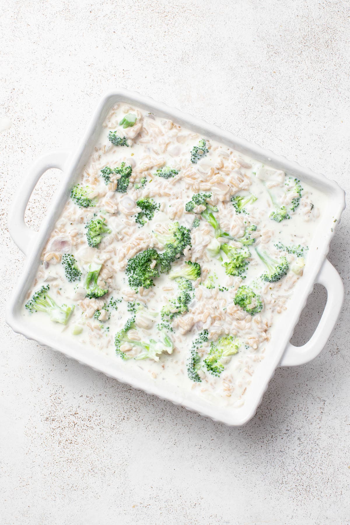 Brown rice and broccoli with the cheese sauce inside a baking dish.