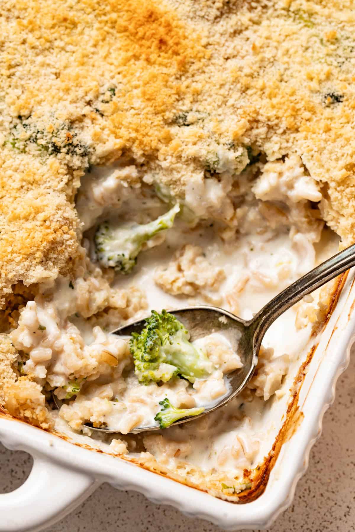 A spoon dipping into the cheesy broccoli rice casserole with a fresh broccoli floret on top.