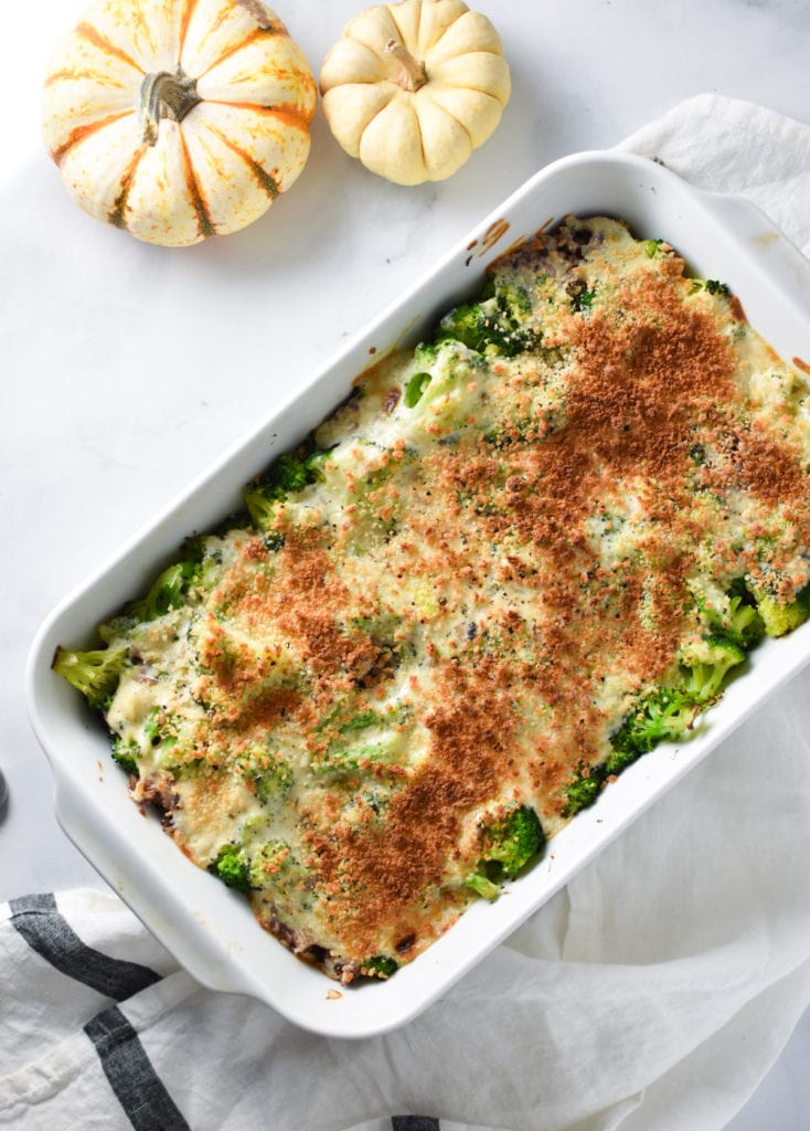 Broccoli rice casserole in a white dish next to white and orange pumpkins