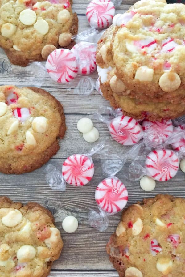 White chocolate and peppermint cookies on a wooden table with peppermint candies and white chocolate pieces