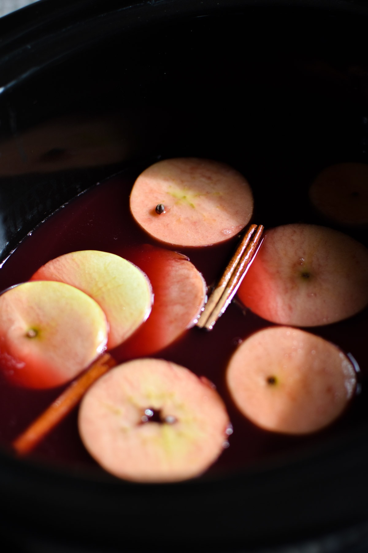 Apples and cinnamon sticks floating in wassail in a crock pot.