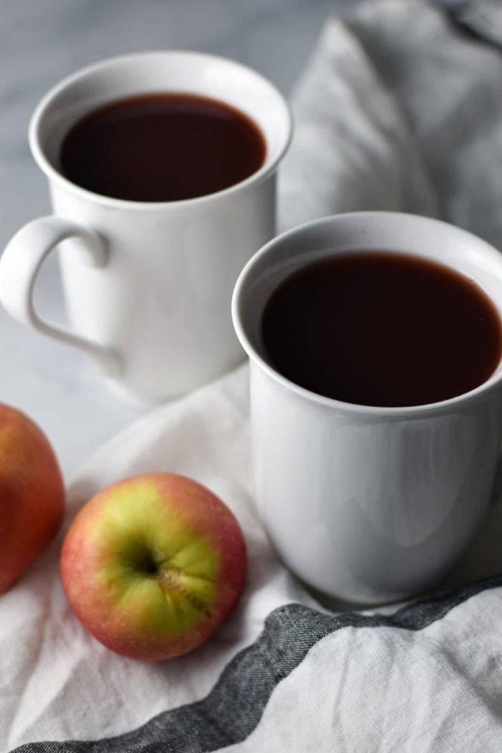Two cranberry wassail cups with apples on a white table