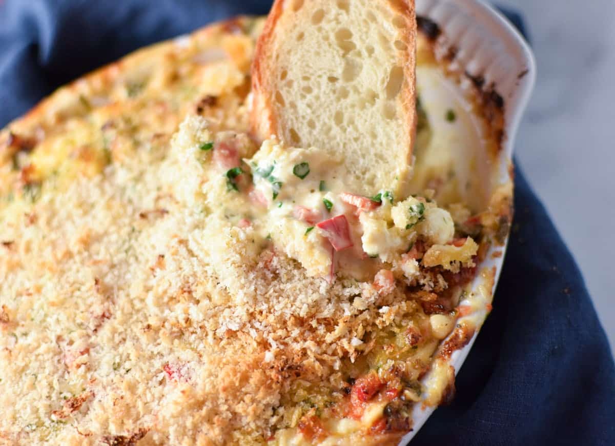 A slice of bread dipping into creamy crab dip