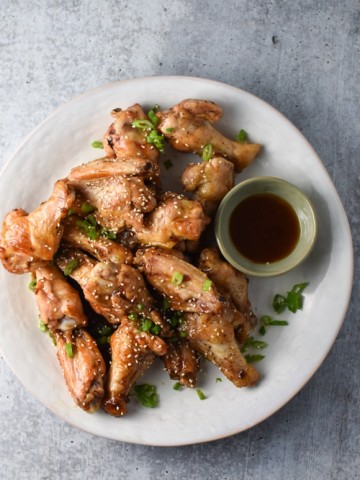 Sesame chicken wings with a dipping sauce and scallions on a grey table