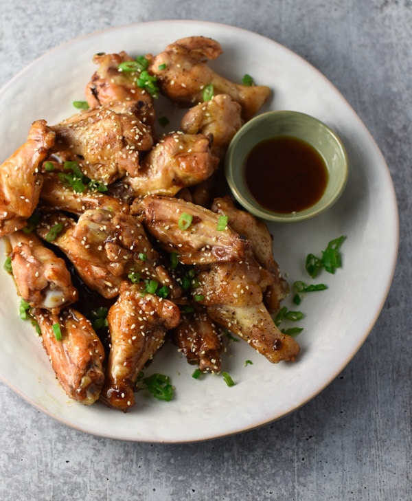 Sesame chicken wings topped with sesame seeds and scallions on a white plate with dipping sauce