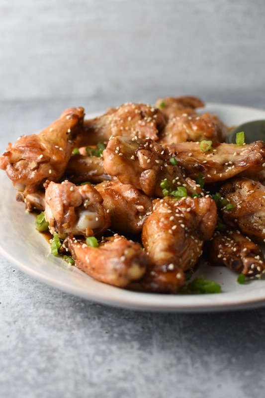 A plate of sesame ginger chicken wings on a grey table