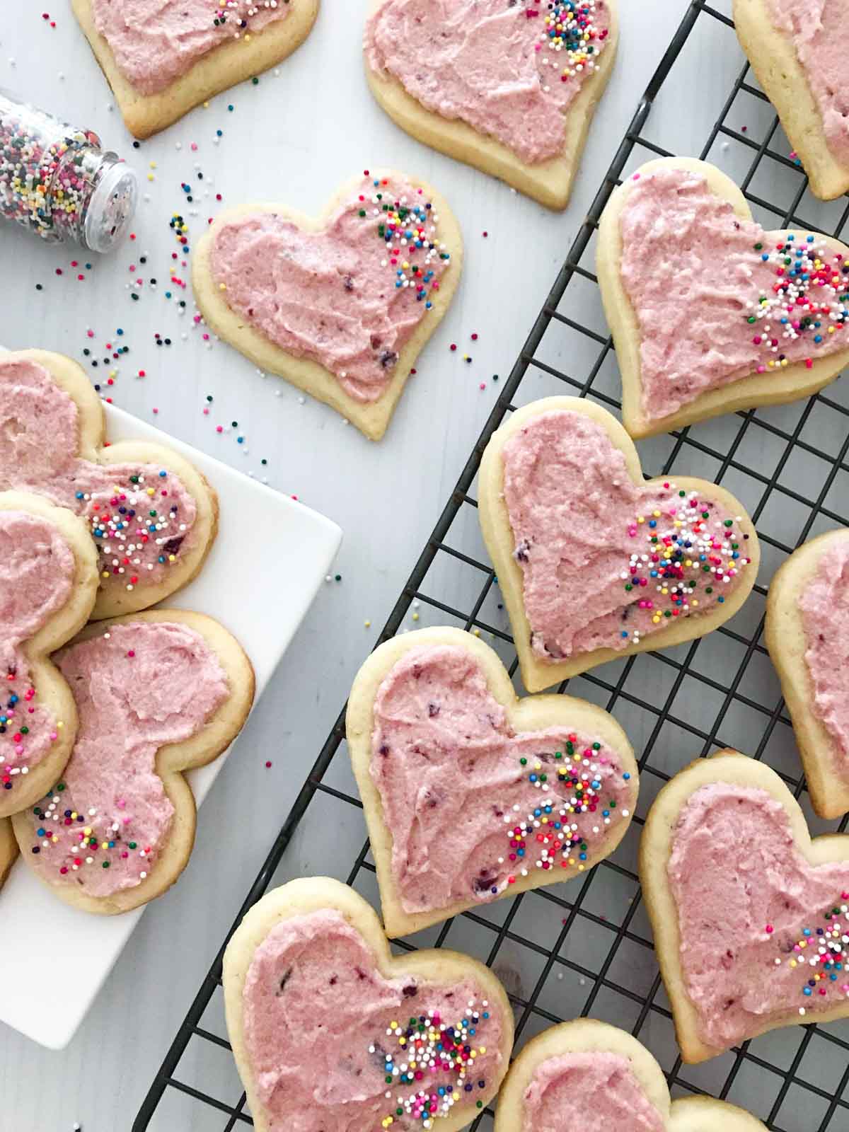 Up close shot of Valentine's Day heart cookies on a cookie rack, being decorated with cherry icing and sprinkles