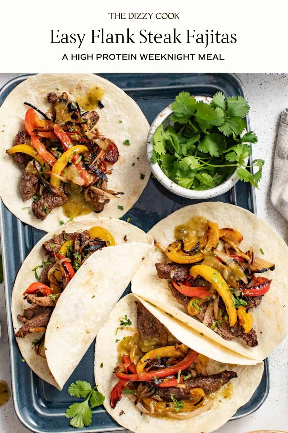 Flank steak fajitas topped with cheese, sour cream and sliced avocados on a gray sheet pan.