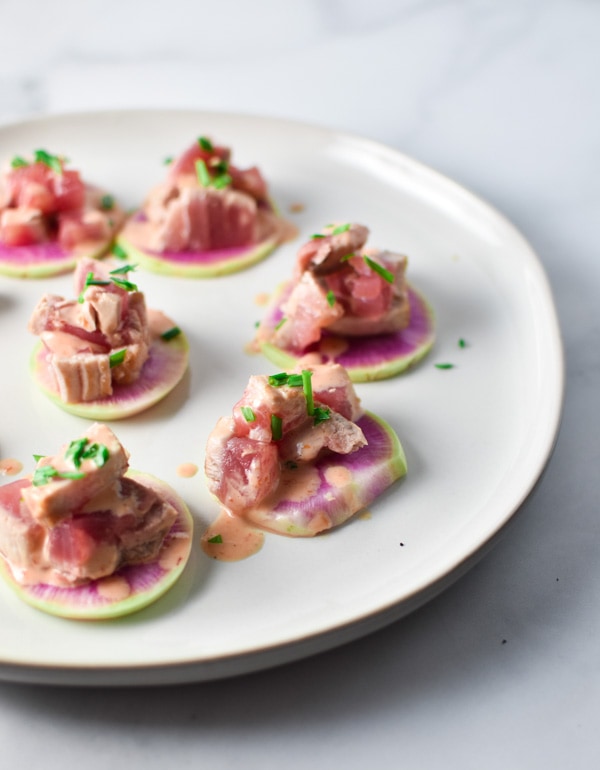 Seared tuna dripping with spicy mayo and topped with chives on a plate