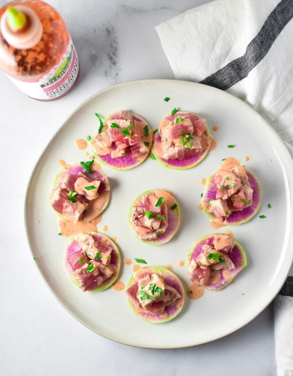 Spicy tuna on top of watermelon radish arranged on a plate with a bottle of hot sauce