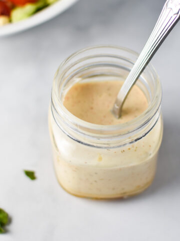 A mason jar with honey mustard ranch and a spoon inside with chopped parsley on top