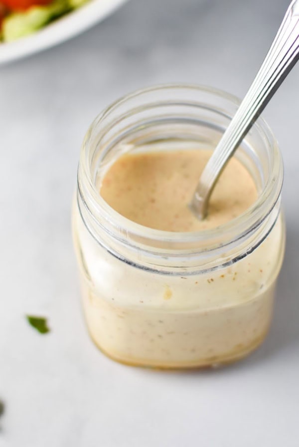 A mason jar with honey mustard ranch and a spoon inside with chopped parsley on top