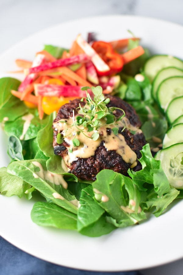 A burger salad topped with spicy mayo and microgreens