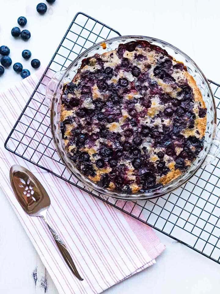 A crustless blueberry pie on a rack with a serving spoon and blueberries