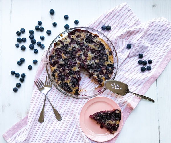 A crustless blueberry pie with a slice cut out and utensils on a pink striped towel