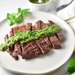 Grilled flank steak with a bowl of chimichurri in the back next to a towel
