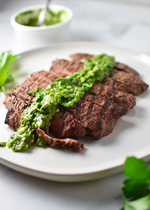 Flank steak sliced on a grey plate with green chimichurri sauce drizzled on top