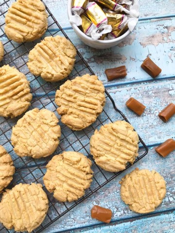 Caramel cookies on a cooling rack with a wood background and candies in a bowl