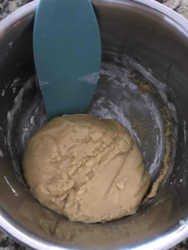 A spatula mixing salted caramel cookie dough to form a ball in a steel bowl