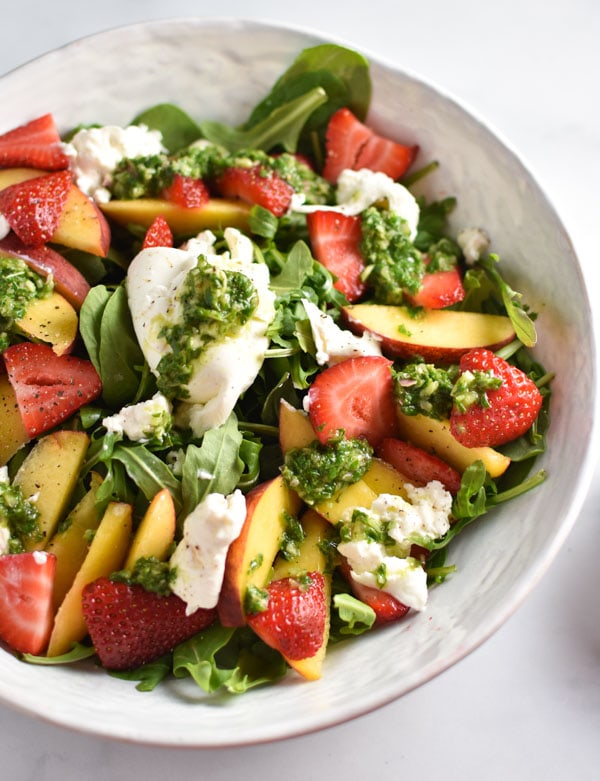 Burrata on top of a strawberry peach salad covered in a basil vinaigrette