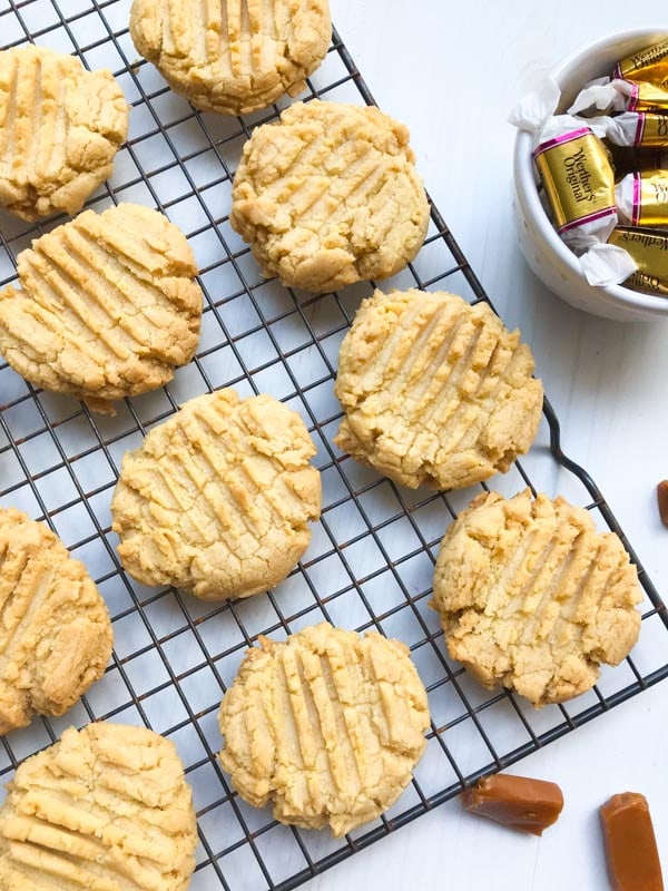Salted caramel cookies on a cooling rack with caramel candies and a white background
