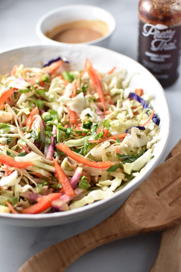 A large bowl of Thai noodle salad with carrots and peppers next to sweet chili sauce