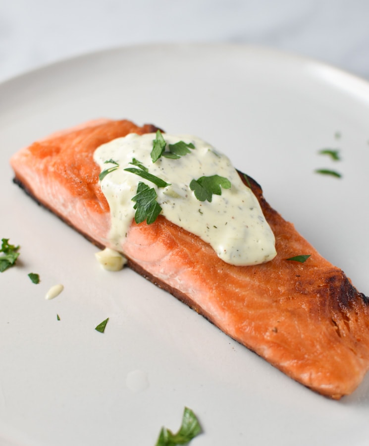 Seared salmon topped with tartar sauce on a grey plate