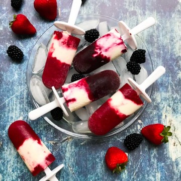 Popsicles on top of a bowl with ice cubes and wooden background with strawberries and blackberries
