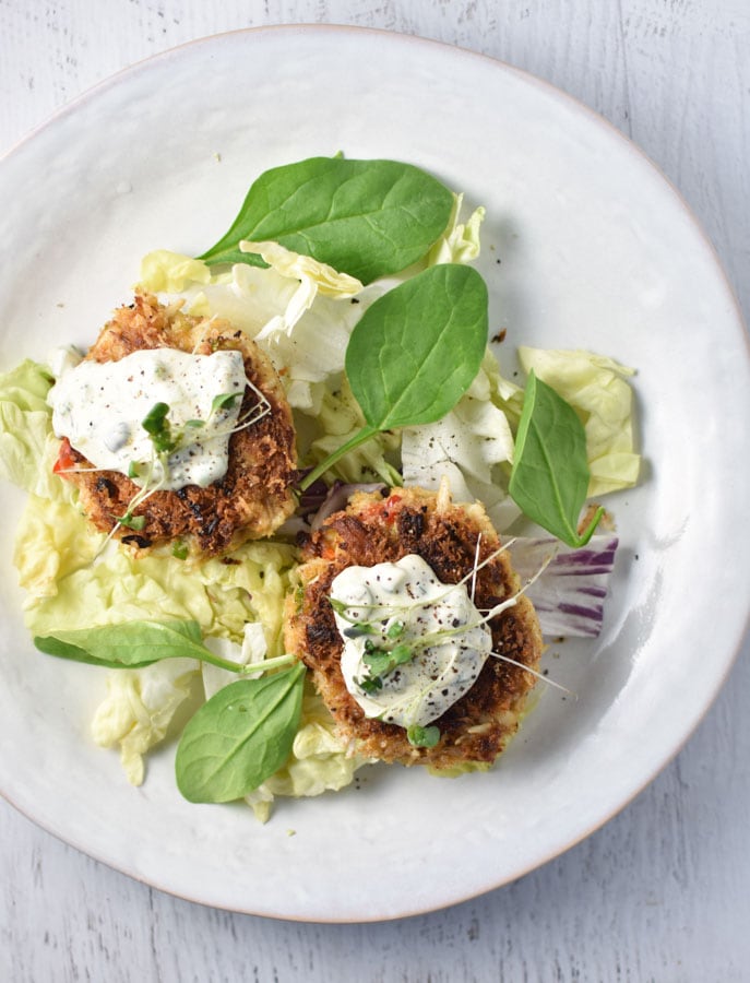 Two crab cakes topped with tartar sauce on a white plate