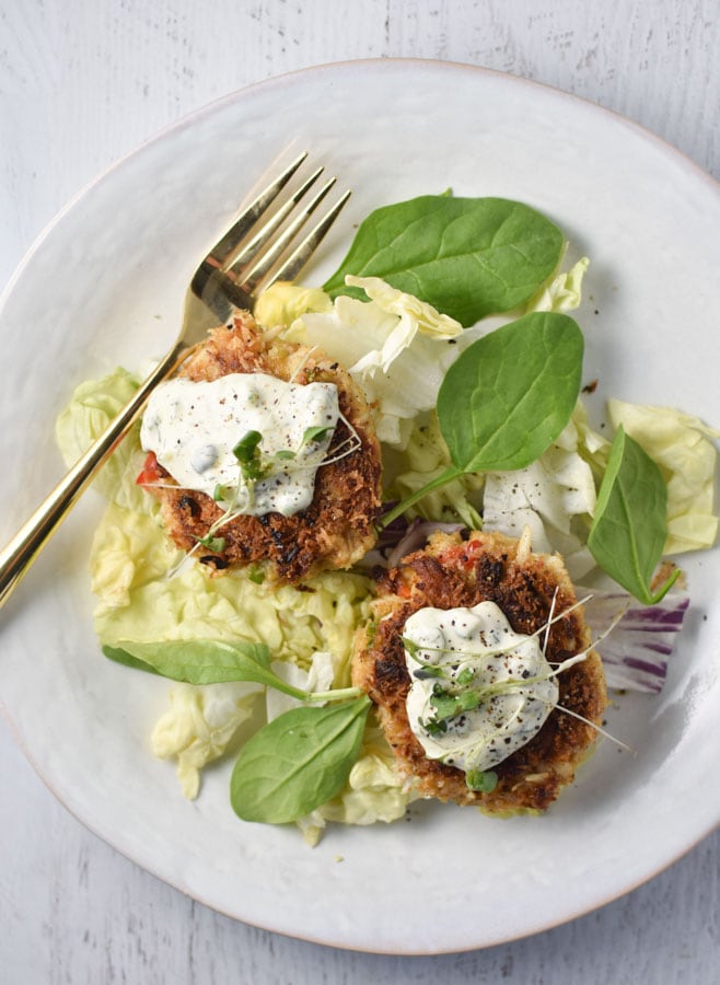 Two crab cakes with a gold fork on a white plate