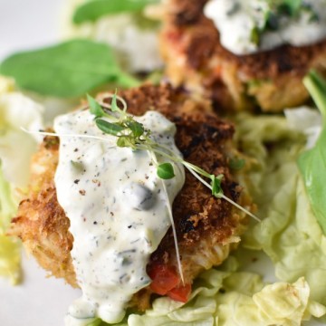 Close up of crab cakes with tartar sauce dripping down on a bed of lettuce