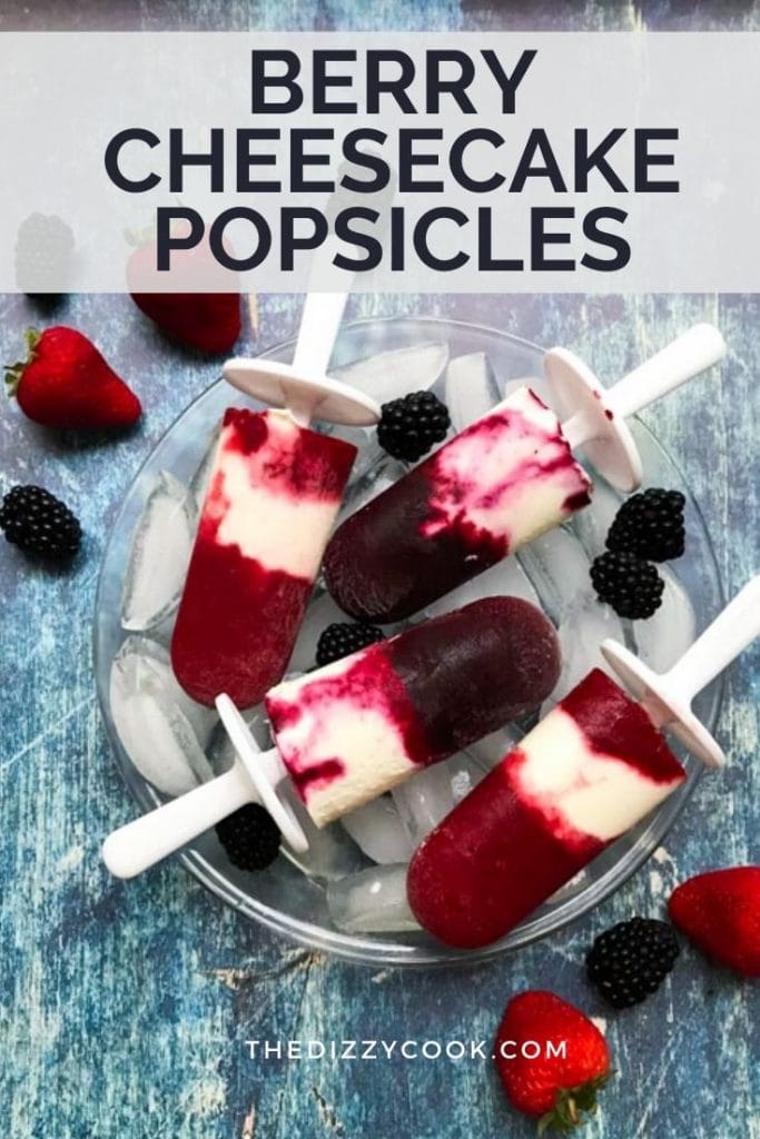Four cheesecake popsicles layered with berries on a wood table