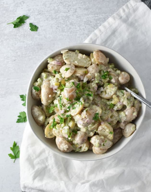 Potato salad in a bowl with a white towel and parsley