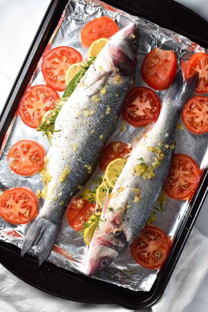 Fresh branzino stuffed with herbs and lemons surrounded by tomatoes