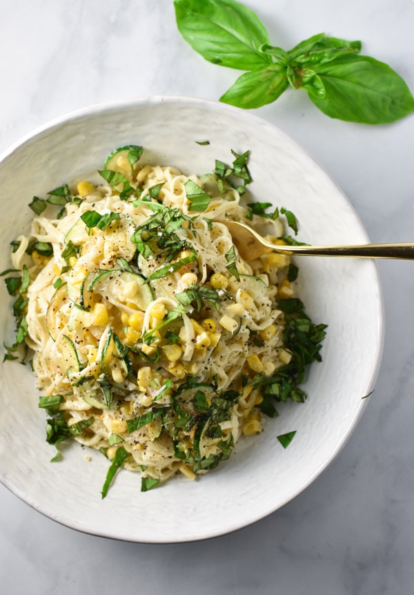 A white bowl of creamy corn pasta with basil on top 