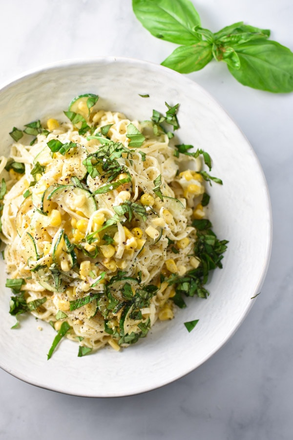 Sliced zucchini, corn, and basil, on top of a bowl of creamy linguine pasta 