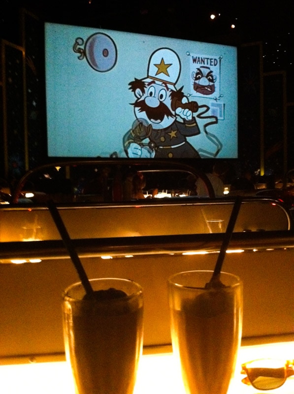 Two milkshakes in front of an old movie at Sci-Fi Dine In Theatre.
