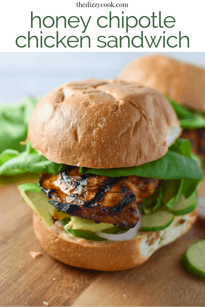 Up close of honey chipotle chicken sandwich with cucumber, lettuce, and shallots on a wood board