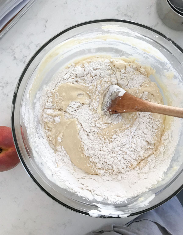 Cake batter being mixed next to peaches on a white surface