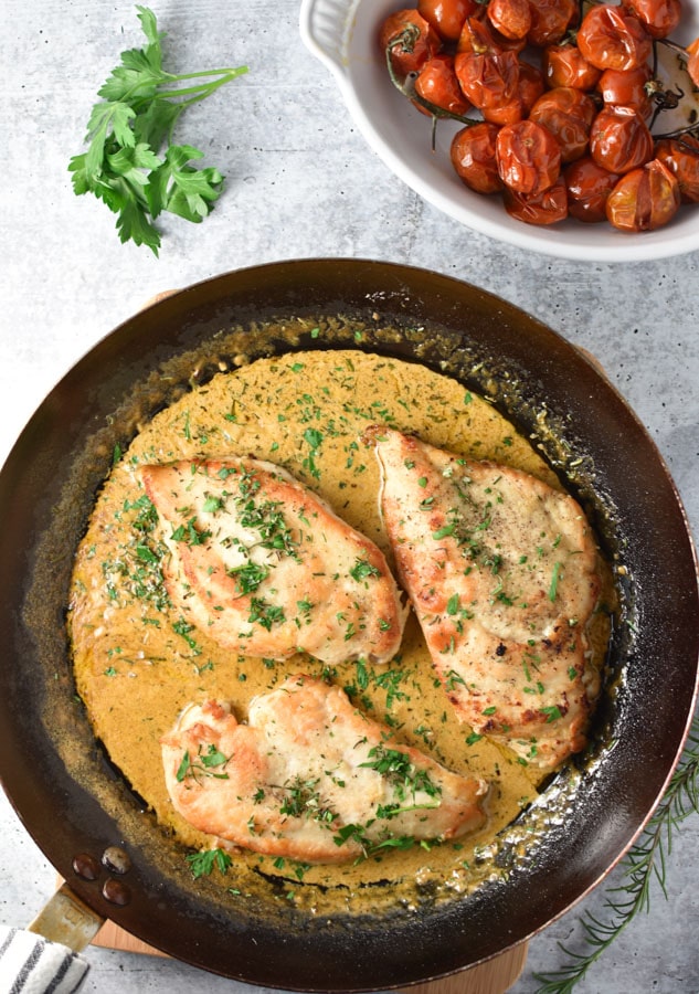 chicken breasts in a pan with cream sauce and tomatoes in a small white dish
