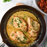 chicken breasts in a pan with cream sauce and tomatoes in a small white dish