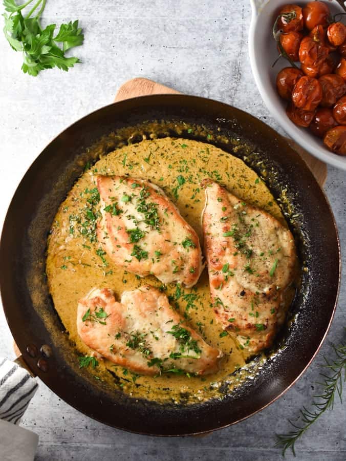 chicken breasts in a pan with cream sauce and tomatoes in a small white dish