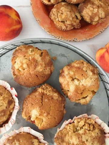 Light brown muffins on a orange plate surrounded by peaches and ginger