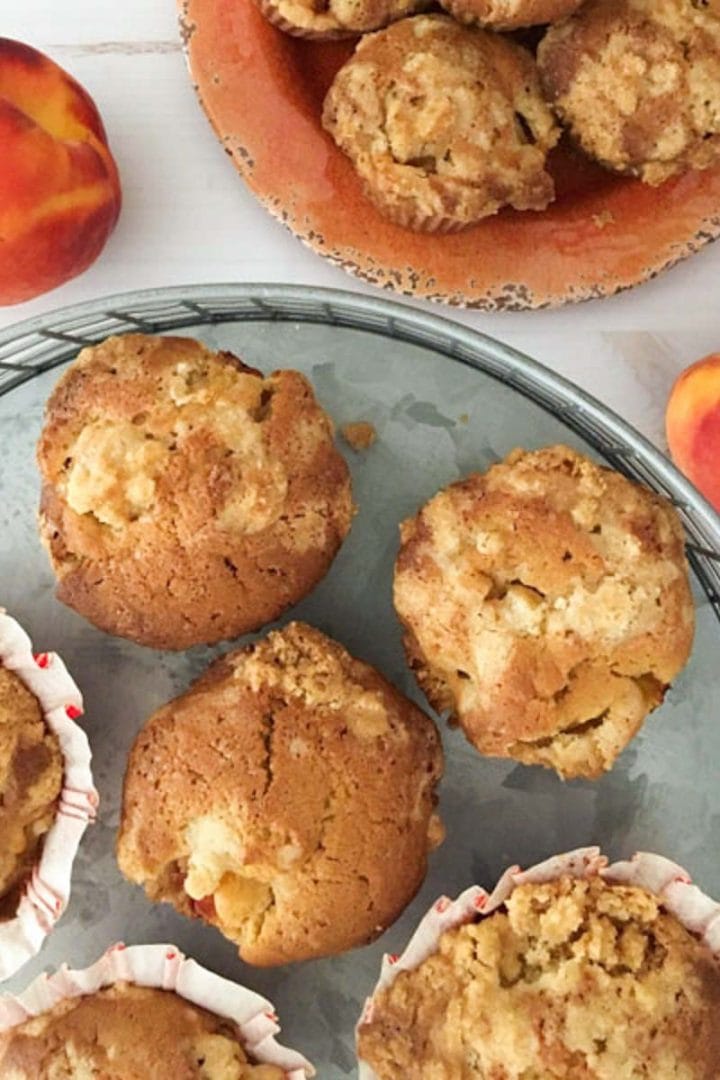 Light brown muffins on a orange plate surrounded by peaches and ginger