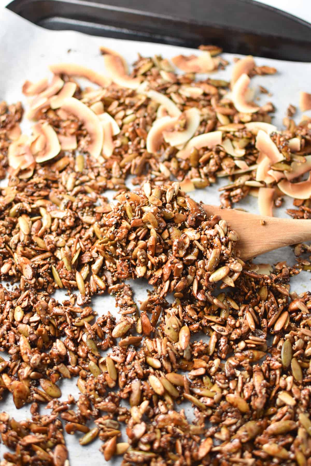 Granola after baking in the oven being scooped up with a spoon.