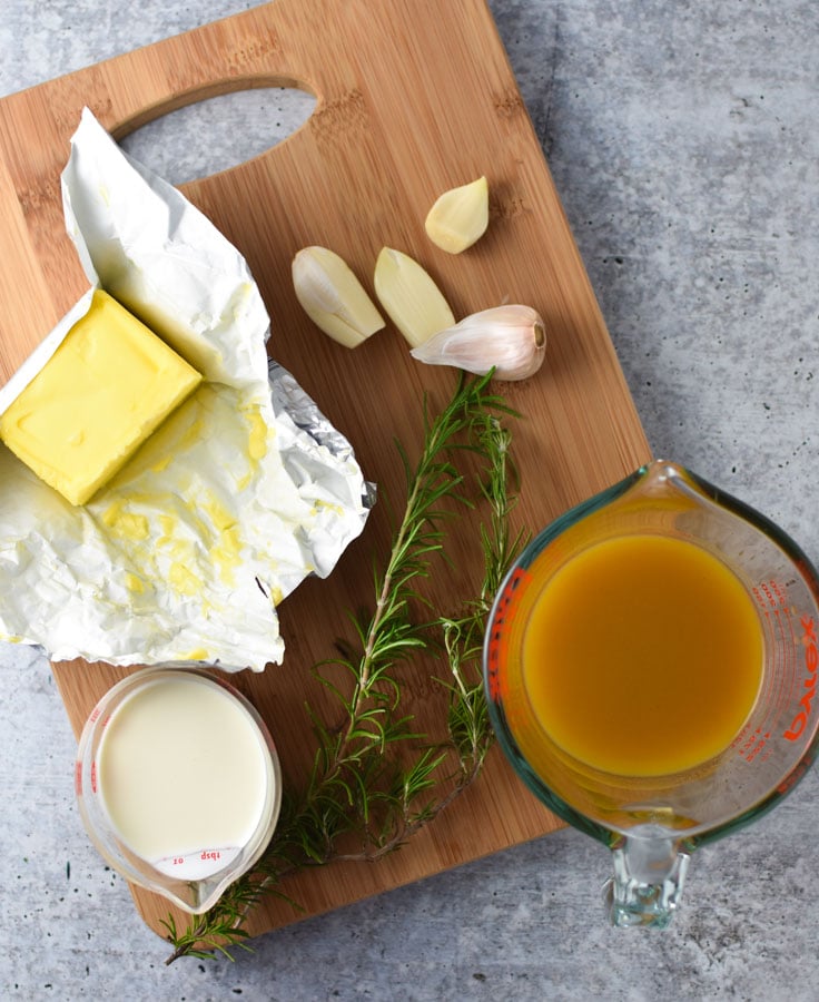 creamy chicken ingredients like garlic, broth, and cream on a wooden board