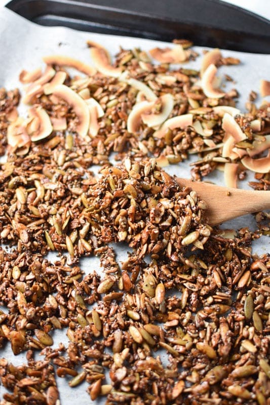 Nut free granola being mixed with a wooden spoon on a sheet pan after baking