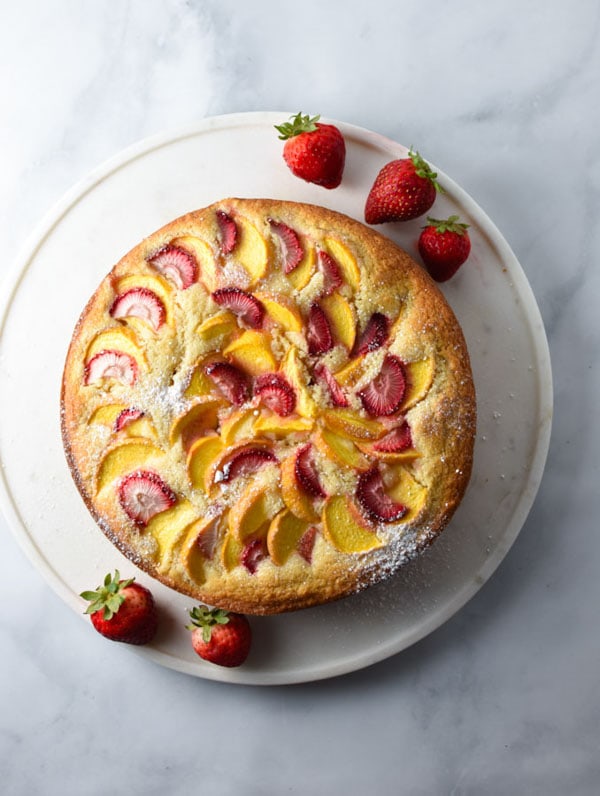 A picture of vanilla cake with layered strawberries on a white marble table