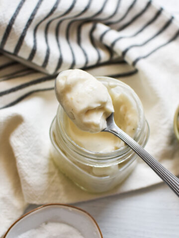 A spoon with eggless mayo on it resting on top of a mason jar.